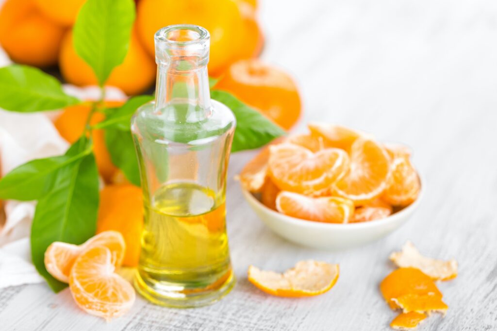 Tangerines with leaves and bottle of essential citrus oil on a white background